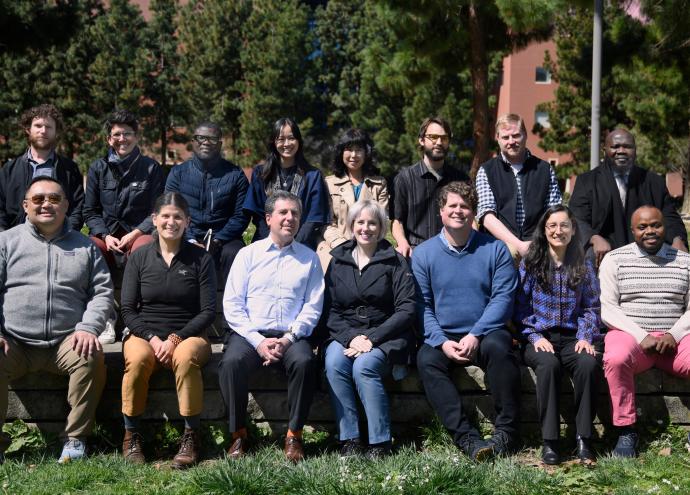 Staff of Spiritual Services sitting in two rows on a bench in a green field. 